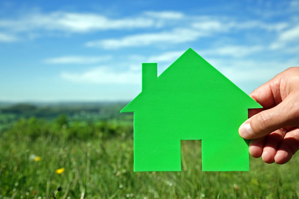 Real estate housing development concept hand holding green house symbol in a field
