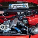 a red sport car's engine with the hood up and a person's blurred hand moving over it for repairs