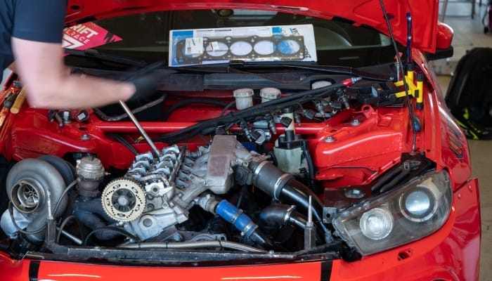 a red sport car's engine with the hood up and a person's blurred hand moving over it for repairs