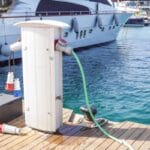 A charging station on a dock next to a boat and two boat motor batteries on the ground next to it.
