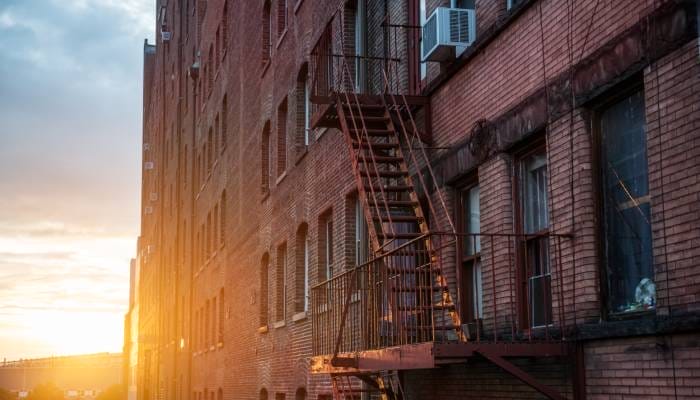 An old and rusty fire escape attached to a red brick apartment building with a sunset in the background.