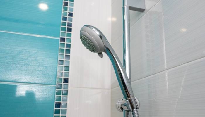 A silver adjustable showerhead on a wall. The shower tile is light blue with small blue and green squares.