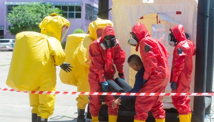 Five firefighters in two different kinds of hazardous materials suits are seen working together during a rescue drill.