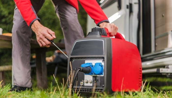 A man firing up a portable red generator on the grass next to an RV by tugging on the pull cord.