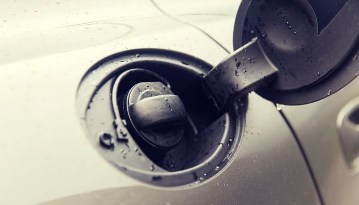 A close-up of a car's open fuel tank, with water droplets around the opening while the safety cap remains locked.