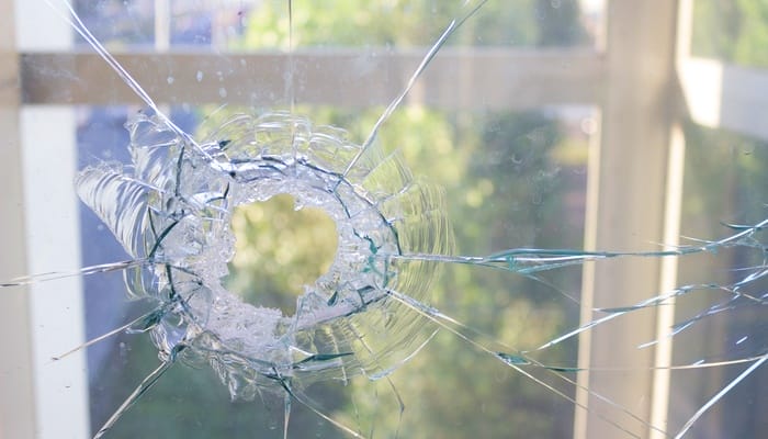 A shattered window featuring a large hole with cracks radiating outward in all directions, providing a glimpse of the outside.