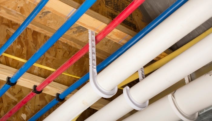A plywood ceiling with thick white plastic pipes secured to it with plastic hooks extending from above.