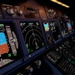 The electronic system in the cockpit of an aircraft. There are buttons and screens displaying flight paths and radars.