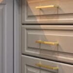 Close-up of gray kitchen drawers that feature gold handles. A cabinet door is right next to the drawers.