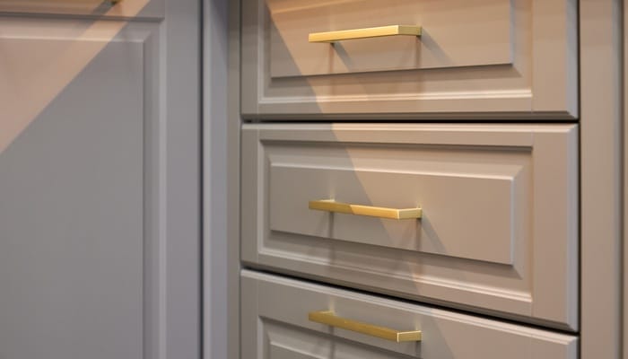 Close-up of gray kitchen drawers that feature gold handles. A cabinet door is right next to the drawers.