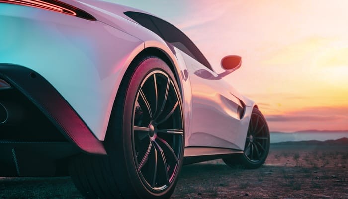 The back of a sports car parked on a hill, looking out at the sunset. The sunset colors are reflected off the vehicle.